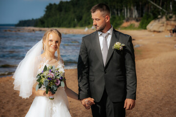 The bride and groom gaze warmly at each other while standing on a sandy beach with gentle waves and...