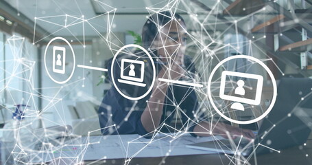 Speaking woman typing on laptop at office desk, with smartphone, documents, pen and network overlay