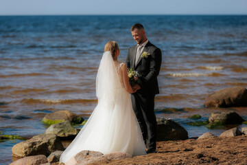 Bride and groom share a quiet, emotional moment on a rocky beach with gentle waves and balanced...