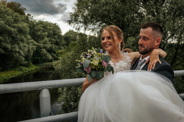 Bride and groom share a heartfelt kiss outdoors, surrounded by lush greenery, as the bride holds a...