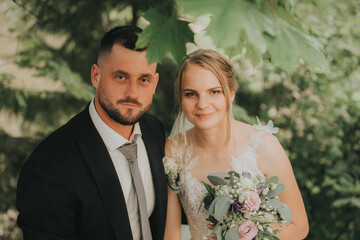 Groom gently holds his brides face as they gaze into each others eyes, surrounded by greenery and...