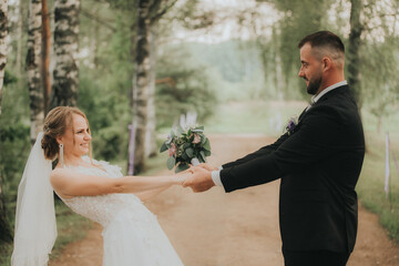 Bride and groom smiling and holding hands playfully on a tree-lined path, celebrating their love in a romantic outdoor setting.