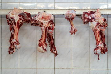 Raw meat bones hanging on metal rail in butcher shop, traditional meat processing and culinary ingredient display on tiled wall