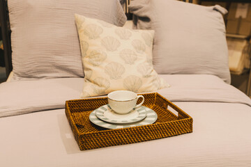 A wicker tray with plates and a cup on the bed.