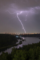Lightning in the sky above the forest during a summer thunderstorm