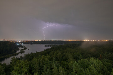 Lightning in the sky above the forest during a summer thunderstorm