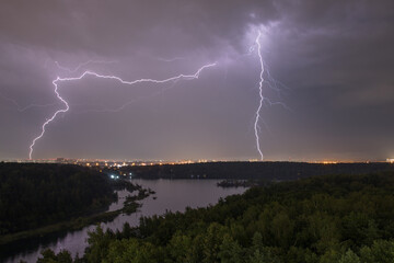 Lightning in the sky above the forest during a summer thunderstorm