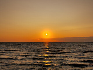 Beautiful sunset over the sea. The sun sets on the water. The sky is painted with bright colors. Summer evening. Sunset beach