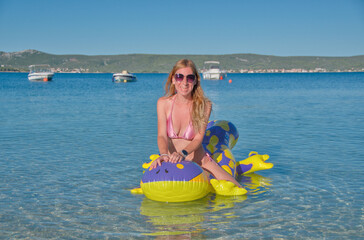 young beautiful woman in sunglasses happily swims early in the morning on an inflatable toy...