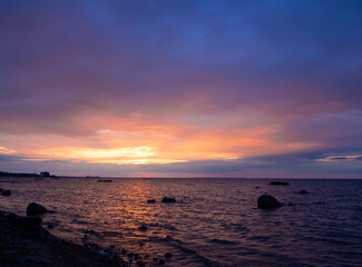 Scenic sunset at the beach in pink shades. The waves are rolling on the shore. Cloudy summer evening.