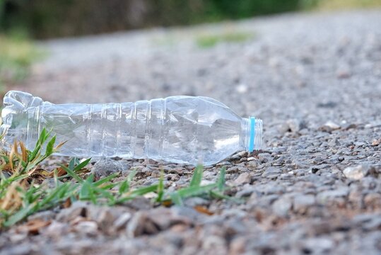 A plastic bottle of drinking water littering on  pathway with green field background,for saving an environmental concept 