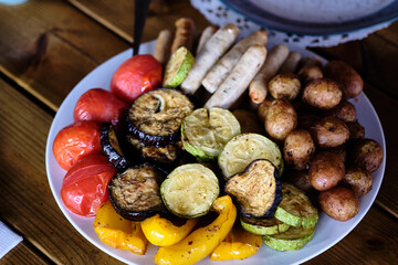 Colorful platter of grilled vegetables and sausages served at a rustic outdoor setting during a...