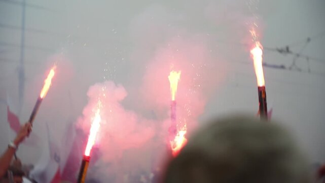 People commemorate Warsaw Uprising Day with red smoke flares during a peaceful march. Polish flags and the uprising symbol are visible through the smoke-filled square.
