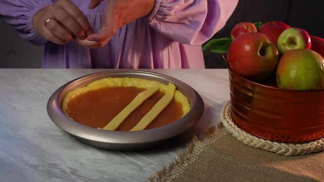 Woman arranging pastry strips on pie with apples in cozy kitchen setting