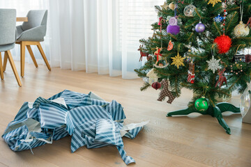 Ripped striped wrapping paper lies near artificial plastic Christmas tree. A contrast of holiday...