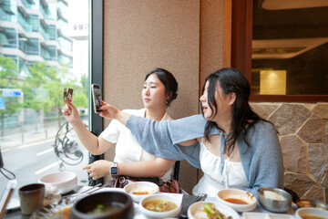 In a kalbi barbecue restaurant at a sunlit window table, two Korean women in their twenties in...