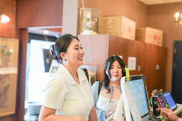 Two Korean women in their twenties in casual clothes pay at the register in a kalbi barbecue...
