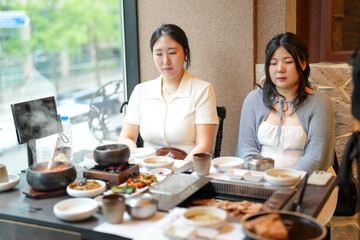 In a kalbi barbecue restaurant at a sunlit window table, two Korean women in their twenties in...
