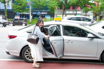 Two Korean women couple in their twenties in casual clothes step into a taxi on a busy boulevard,...