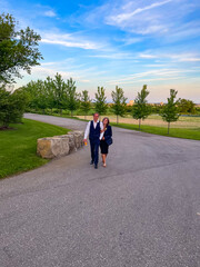 A well dressed young couple walk down a road on a farm at sunset. The girlfriend has her boyfriends...