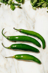 four green serrano peppers on white marble with cilantro to the side, mexican food