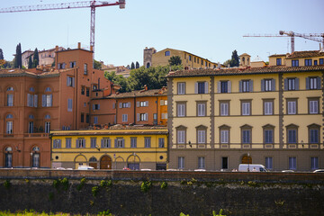 Fototapeta premium Historic riverfront architecture with bright facades and shuttered windows framed by hillside homes Florence Italy