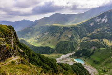 Fototapeta premium A scenic Caucasus vista showcases rugged peaks and lush valleys, with a small turquoise lake near Gudauri, Georgia.