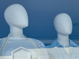 Close-up of faceless fashion mannequins in modern clothing store window with minimalist style and...