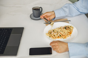A person happily relishing a delicious bowl of pasta while efficiently working on a laptop and...