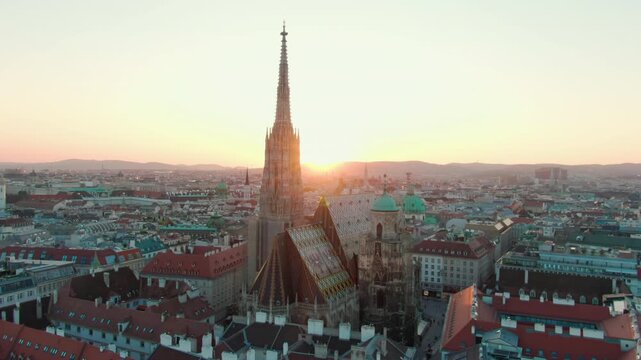 Drone footage of St. Stephens Cathedral in Vienna during sunset, with warm light on rooftops and spire. An iconic Austrian landmark in golden hour for cinematic or travel footage. 4K aerial panorama
