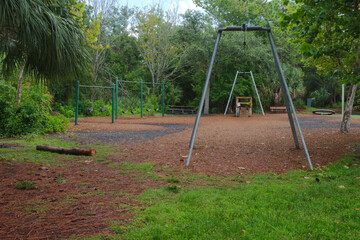 Empty Playground Amid Green Surroundings and Trees After Rainy Weather in nature park. Quiet playground with swings and climbing structures, encircled by vibrant greenery under a damp environment afte