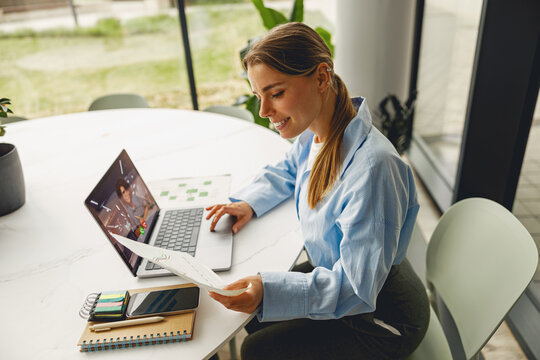 A young woman diligently reviews important documents while working on her laptop in a stylish and modern office space