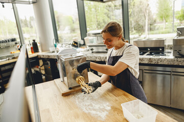 A young woman is skillfully preparing fresh pasta in a bright, stylish contemporary kitchen...