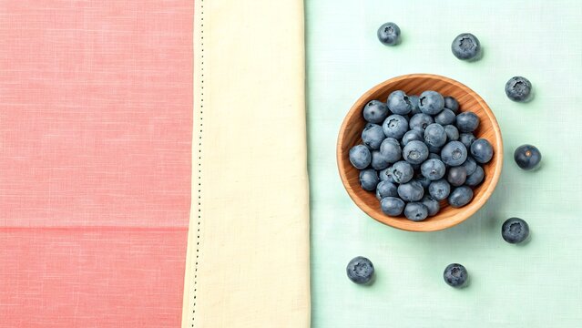 Wooden bowl filled with fresh blueberries on a colorful wooden surface - Powered by Adobe