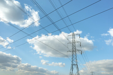 Electricity pylon or tower with power lines running across a blue sky with clouds