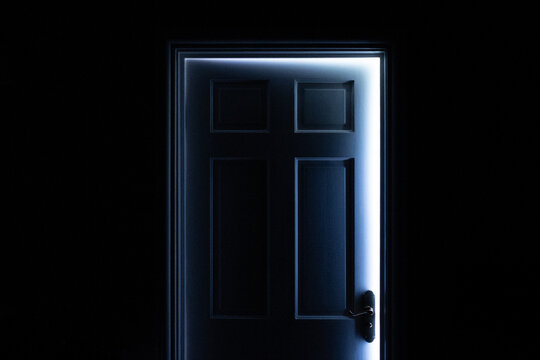 Slightly open or ajar door letting in daylight against a totally black foreground with space for text or copy