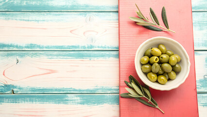 Green olives in a bowl on a red board and blue wooden table background