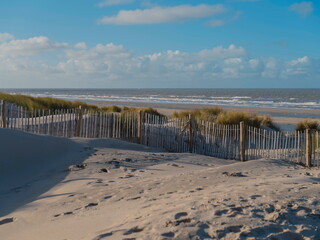 Coastal sand dunes with wooden fence protection and footprints leading to ocean beach