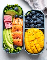 Top-down view of a vibrant lunch box filled with salmon, mango, fresh tuna, cucumber, and blueberries—healthy, colorful, and delicious.