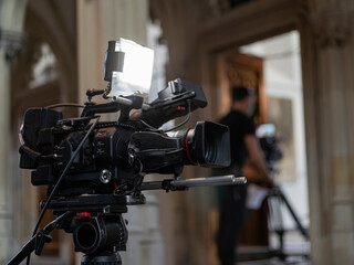 High-end video camera mounted on tripod in architectural interior with columns and arches