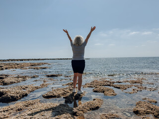 Senior tourist woman enjoying seaside view and taking photo with smartphone during vacation travel