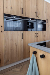 Kitchen wall featuring built-in oven, microwave and coffee machine integrated into light wooden...