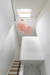 Staircase with natural lighting from skylight above, featuring copper pendant lights and modern...