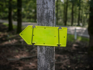 Yellow directional arrow signs mounted on wooden post providing trail navigation in forest setting