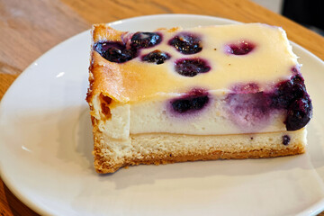Delicious slice of cheesecake topped with fresh blueberries on a white plate
