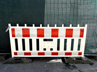 White construction safety barrier with red and white reflective stripes placed on a road during...