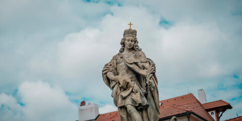 Historic baroque religious statue with cross against cloudy sky in Prague