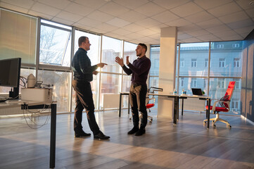 Two Caucasian men talking at work in the office. 