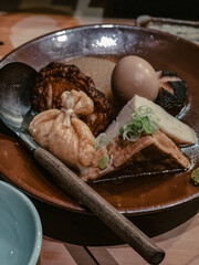 Close-up of a traditional Japanese oden dish with assorted simmered ingredients including egg, tofu, radish, and fish cake.