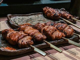 Grilled Japanese yakitori skewers wrapped in bacon, displayed on rustic ceramic plates in a cozy izakaya setting.